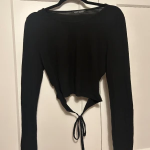 Cropad tröja med knytning i ryggen  - En svart cropad tröja med knytning i ryggen, fin men har lite små knottror men inte något man tänker på och på  snöret har sömmen gått upp lite men syns inte heller om man inte kollar noga