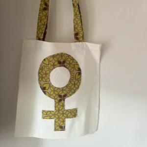 Tygkasse, tygväska, tygpåse  - Handsydd tygkasse med motivet ”feminist”.   Tillverkad i 100% återvunna textilier.   Mått: 32x35 cm  Hämtas på Södermalm alternativt skickas med post. 