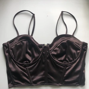 Brun Korsett silkestopp - En mörkbrun korsett i silkes material med justerbara band och dragkedja. Jätte fint skick, aldrig andvänd. Stl. 42 men passar även mindre storlekar eftersom den är stretchig. Jag som oftast har 34/36 kan andvända den den blir bara lite stor i kuporna.💕💕