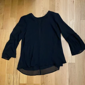 Svart blus, Storlek 34 - Använd 1 gång för ca 1/2 år sen. Köpt från Gina Tricot i storlek 34. En tunn svart blus med lite volanger vid ärmarna och en knapp på baksidan vid kragen som går att knäppa upp. 