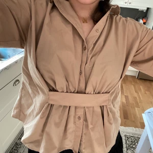 NA-KD topp - beige skjort-liknande topp från NA-KD😍 köpt för ca 2 år sen men använd 2-3 gånger, man kan öppna alla knapparna