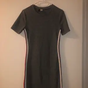 Grå klänning i storlek 40 från H&M! Bekväm längd men relativt kort, har två vita och röda ränder på sidan! Otroligt skönt material!
