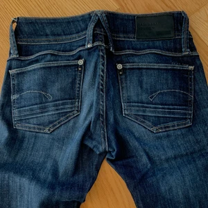 Lågmidjade mörka blåa jeans med snygga detaljer - Ett par lågmidjade mörkblåa jeans som med en urtvättad effekt och gula sömmar. Jeansen är från 1900-talet. Jeansen är från G stat och köpa för ungefär 1200kr. Startar budgivning på 400kr. Storleken är W 26 L 32. 💛