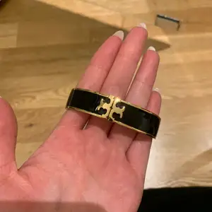 Oanvänt armband från tory burch i svart och guld. Armbandet öppnas i mitten vid märket så den passar armleder i olika storlekar. 