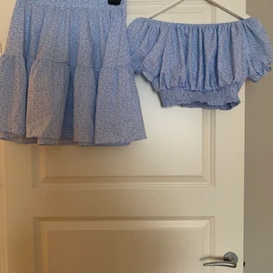 Blått set kjol och topp - Ett blått blommigt set med kjol och off shoulder topp i storlek L. Passar även M. Finns i Mölndal/Göteborg eller skickas med Postnord, köparen står för frakten.