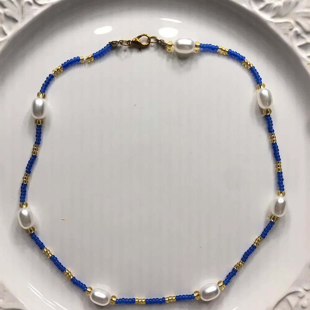 Ett blått och gudligt halsband med vita pärlor.           Du kan själv bestämma länden på ditt halsband. Tråden är elastisk. Förlängningskedja ingår också. Frakt ingår i priset❤️⚡️🙌✨. Accessoarer.