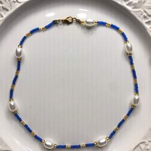 Ett blått och gudligt halsband med vita pärlor.           Du kan själv bestämma länden på ditt halsband. Tråden är elastisk. Förlängningskedja ingår också. Frakt ingår i priset❤️⚡️🙌✨