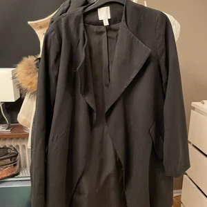 Trenchcoat  - En svart trenchcoat som aldrig är använd.