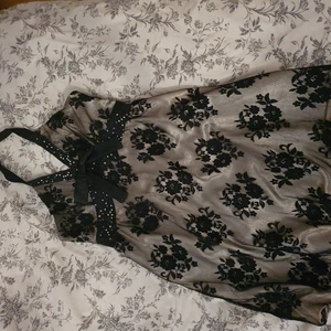 Festklänning i stl. 38 - Helt ny festklänning i stl.38. Halterneck modell. Glansigt champangefärgat tyg med svart spets över. 