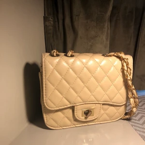 Beige miniväska  - Den eleganta beige och quiltade väskan med gulddetaljer passar både vardag och fest. Axelremmen är cirka 110 cm lång o har använt den några gånger