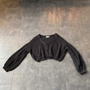 En svart stickad tröja ifrån NA-KD. Den är croppad, svart och i storlek M. Den går även att knäppa upp så att de blir en kofta. Använt fint skick!😙