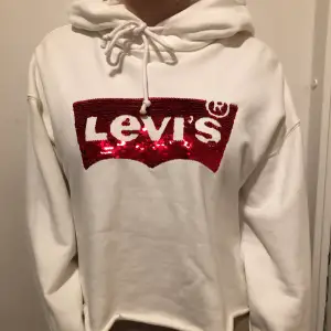 En vit croppad Levis hoodie med vändbara paljetter! Använd en enda gång och är i mycket fint skick! Hoodiens ordinarie pris är 650kr.  🤍🥥🦢