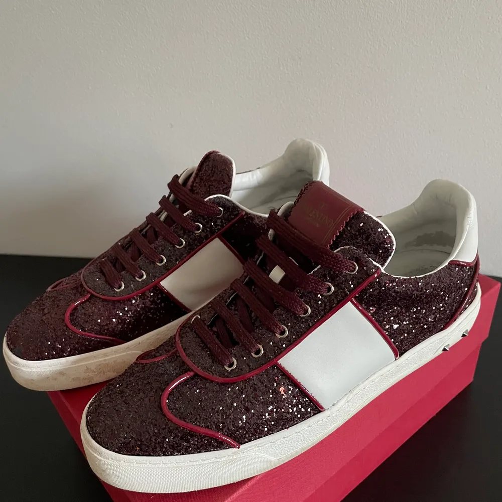 Säljer dessa jätte coola skor från valentino garavani i modellen flycrew med glitter på. Färgen är burgundy (vinröd). De är i storlek 40 men är lite större i storlek. Ena skon har tappat en nit samt lite glitter på ena tån men inget man märker vid användning. Annars i super fint skick! Hör av er om ni vill ha fler bilder så fixar jag det!. Skor.