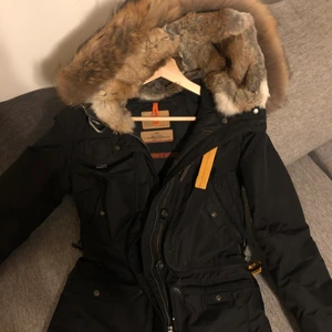 Parajumper jacka storlek S  - Svart dunjacka från Parajumpers. Jackan har flera praktiska fickor och luva med avtagbar naturpäls inuti luvan och på kragen, båda är avtagbar. Patch med logotyp på vänster ärm. Stort spänne vid kragen. Stängs med dragkedja och knappar. Ingår i Parajumpers Masterpiece Series bestående av deras exklusivaste modeller! Jackan är köpt för 3 år sedan men användes nästan aldrig, och är därför i gott skick. Värde 10 499 kr! 