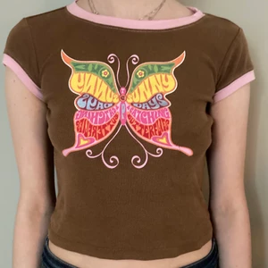 Brun babytee med fjäril  - Brun babytee med en regnbågsfärgad fjäril med text. Använder aldrig denna vilket är så synd med tanke på hur fin den är:-( frakt 37kr💕