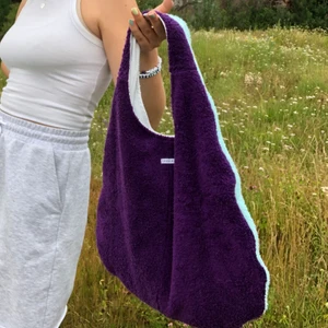 Lila och mintblå handgjord frottéväska  - En så ball lila och mint-blå frotté väska i modellen ”Karin” med vit insida med två djupa fickor. Väskan går att vändas ut och in, se bild 3, om man bara vill ha en vit väska. Perfekt väska som ger dina outfits det lilla extra men samtidigt är extremt rymlig. 