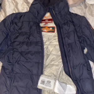 Parajumper  - Parajumper jacka (mörk blå) (äkta) i bra skick men lite sönder vid inne fickorna men går att laga. En väldigt bra vårjacka.        Skicka för fler bilder. Köpt på kidzbrandstore i storlek 14. Vid snabb affär kan jag sänka priset