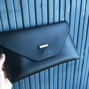 Portmonnäväska - En portmonnäväska i svart skin ca 30x20cm stor. Jag har haft den som en handväska i handen men det finns möjlighet att sätta på ett axelband.