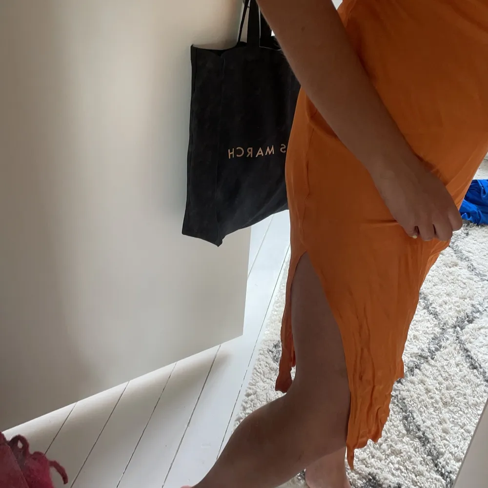 Knälång klänning i jättefin orange färg med knytning i ryggen och slits på vänster sida . Klänningar.