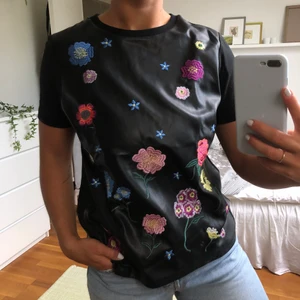 Skinn t-shirt med broderade blommor  - Supercool skinn t-shirt från Zara med broderade blommor i olika storlekar och färger. Framsidan är i läderimitation medans armarna och baksidan är gjort av tyg. 