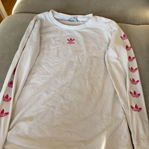 Adidas tröja  - En långärmad adidas tröja med rosa adidas tecken längst armarna och ett adidas tecken mitt på tröjan. Säljer denna tröja för att inte använt så mycket. (Äkta adidas)