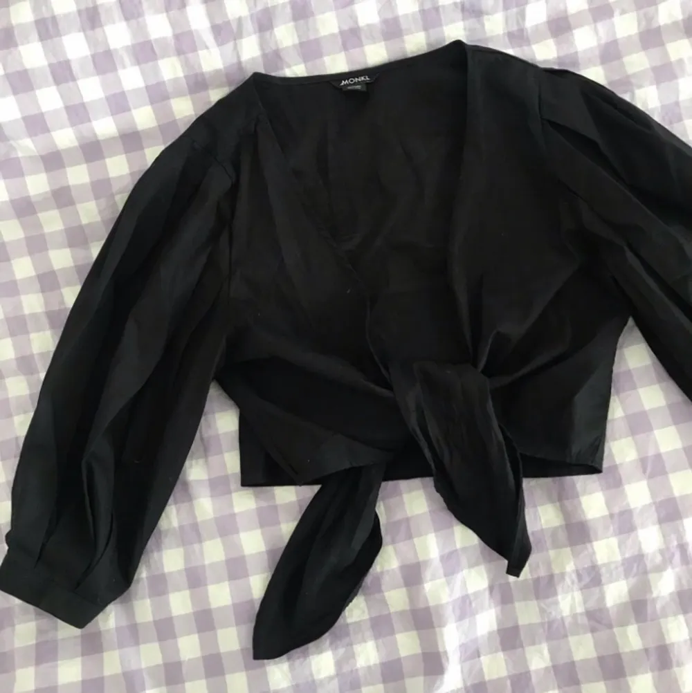 Nästan oanvänd svart tie-front blus från Monki. Fin längd och puffiga ärmar. Säljer för att den inte passar mig🌸. Blusar.