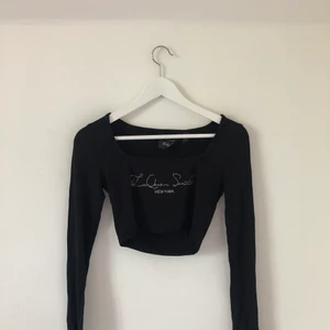 Kort, svart topp med glittrig text  - En cropped svart topp med långa ärmar och fyrkantigt formad ringning. Någonting som jag tyvärr inte riktigt kan tyda✨ står över bröstet med glittriga stenar.