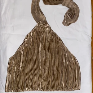 Festtopp med öppen rygg - Jättefin festlig topp med öppen rygg och knyte runt halsen/nacken. Glittrig guld med knäppning bak. Aldrig använt, men var dum som klippte bort prislappen så kunde inte returnera. Passar till storleken!