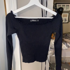 Svart of shoulder tröja med volang  - Denna fina topp kommer från NewYoker och är en väldigt fin basic topp men även till lite festligare tillfällen. Denna är i storlek S men skulle passa en xs också:) 