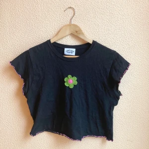 T-shirt från Vintage Supply - T-shirt från Vintage Supply. Aldrig använd! Svart med grönt virkat motiv på bröstet. Rosa sömmar i ärmar och nederdel. Strl L, men relativt liten i storlek. Frakt ingår! 