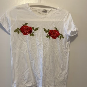 T-shirt med broderi - En vit T-shirt med broderade rosa / röda rosor över brösten. Använd 3 ggr. Från pimkie, köpte den i marbella för något år sendan! Skulle säga att den passar xs och s!