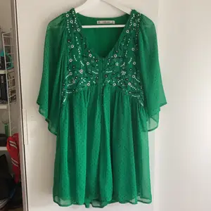 Grön klänning med inbyggda shorts (syns inte pga allt tyg) med söt dekor och små prickar. Använd en gång. Skön och tunn i materialet. Bilden gör inte klänningen rättvis, den är grönare irl. 