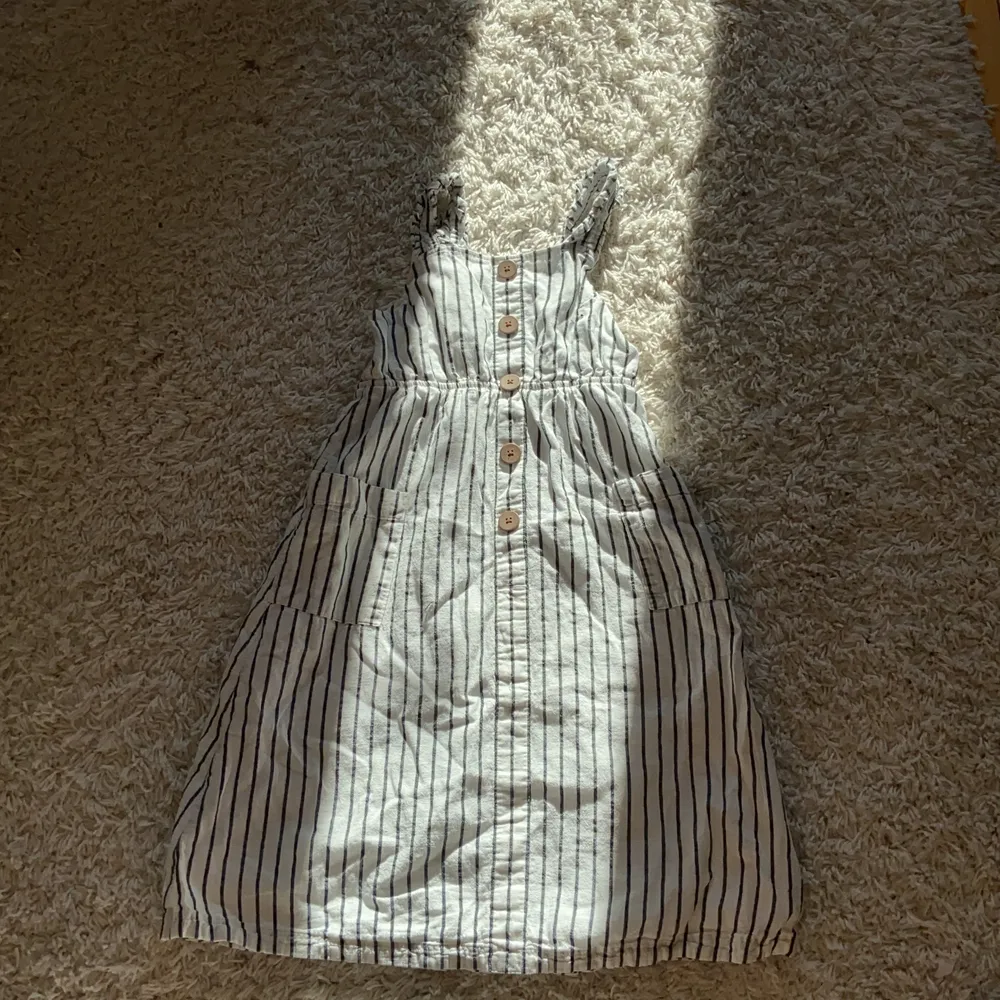 En randig klänning i hyfsat bra skick där jag har använt den hyfsat många gånger, den har stora bruna knappar där fram och det finns även ett vit tyg under kjoldelen, den har även två fickor där fram.. Klänningar.