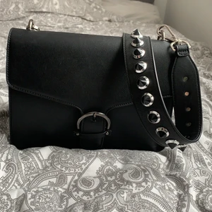 Svart väska med nit axelband  - Svart väska i fakeläder. Väldigt rymlig med många fack och i fint skick. Frakt kostnad tillkommer. 