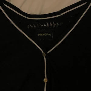 Zadig och Voltaire kofta  - Intressekoll på min fina Zadig och Voltaire kofta. Den är svart med vita deltaljer och guldiga knappar. Den är ylle och är i storlek xs. Säljer endast till bra pris då jag verkligen gillar den. Den är köpt för ganska länge sedan och kommer tyvärr inte till användning lika mycket som den borde❤️❤️🥲 