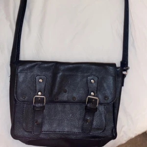 Väska  - En axelväska/ handväska, man kan justera bandet beroende på hur lång man vill att den ska vara. Köpt på second hand för 300 kr. Bandet är ganska slitet men annars är väskan i bra skick. ”Taggarna” är väldigt unika då dom är så vassa och coola.