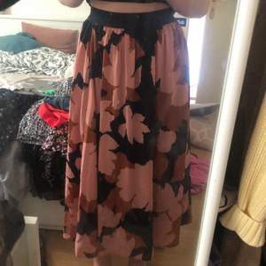 En lång kjol som är brun/beige, rosa och marinblå. Mönster av löv. Kjolen är stretchig i midjan 