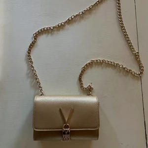 Valentinoväska guld - En guldig kuvertväska med kedjerem från Valentino. Helt perfekt skick, endast använd ett fåtal gånger. Originalpris 800 kr.