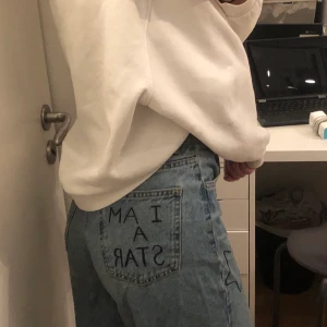 Blå utsvängda byxor med målade stjärnor  - Blå utsvängde byxor med målade stjärnor på framsidan och skriven text på en bakfickan, säljer då de inte används så mycket längre