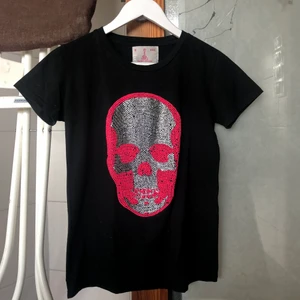 Dödskalle t-shirt  - Dödskalle t-shirt med rosa och silvriga rhinstones! Det är några stenar som saknas men egentligen inget man tänker på. Storlek saknas men sitter som en S/M möjligtvis lite tajt i ärmarna