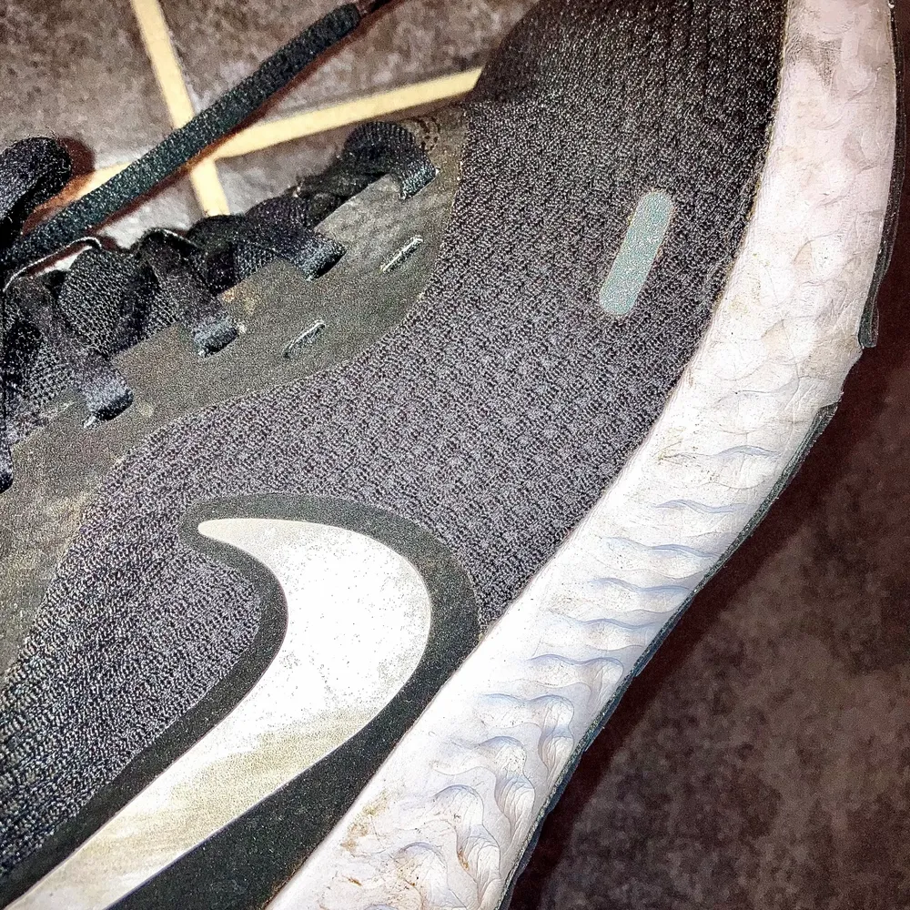 Sportiga sneakers från Nike. Svarta med vita detaljer och en mörkgrå reflex. Skorna har inga skador, men är smutsiga på det vita gummit. Storlek 40, eller 24,5 cm innerlängd.. Skor.