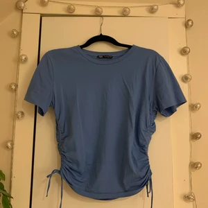 Blå tröja från zara - En superfin blå t-shirt från Zara med ”knyt” på sidorna. Superfin färg till sommaren, den är lite blåare än vad den ser ut på bilden. Säljer då den inte kommer till användning längre. Skulle säga att den är ganska liten i storleken men det beror lite på hur man vill att den ska sitta! Skriv för frågor eller fler bilder etc ❤️‍🔥❤️‍🔥