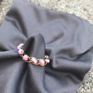 Flätad ring i guld färgad smyckes tråd, med rosa pärlor.                 stl: S-XS.                                                     Den är Nickel fri, Bly fri och Kadium fri!!!