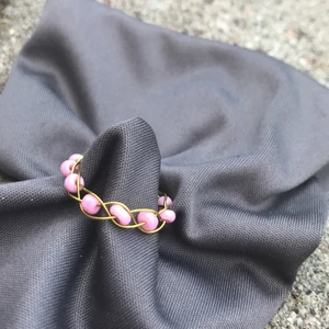 Egengjord flätad ring 💍  - Flätad ring i guld färgad smyckes tråd, med rosa pärlor.                 stl: S-XS.                                                     Den är Nickel fri, Bly fri och Kadium fri!!!