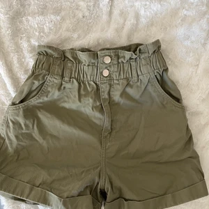 Militär gröna shorts - Shorts med stretchig midja, uppvikta längst ner och silvriga knappar samt dragkedja.