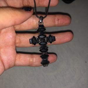 Ett svart halsband med ett kors på och nå slags svarta stenar på