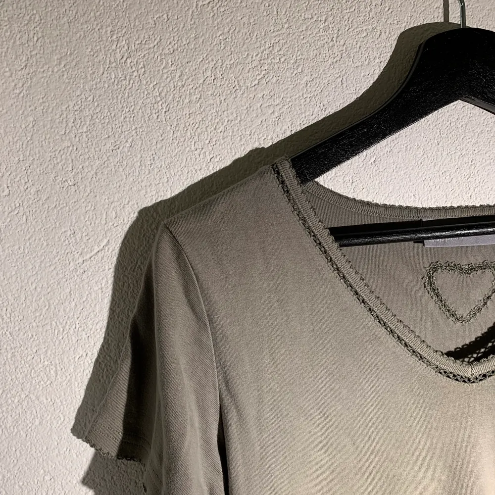 Supersöt grå/grön T-shirt med fina ”spets”detaljer samt ett hjärta i ryggen! Köparen står för frakten💗💗. T-shirts.