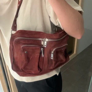 Nunoo väska - Säljer denna jättefina väska från Nunoo. Är i mocha och har en fin mörkröd/rost-aktiv färg. Är i fint skick!