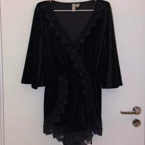 Svart playsuit i sammet - Svart velvet playsuit med spets detalj och wrap v-ringning