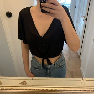 Kort svart topp - Kort, svart, sommar topp. Fyra fejk knappar på framsidan och en liten Knut som går att knyta upp. Naveln syns. V-ringad. Luftiga ärmar. Kan hämtas upp i Vasastan eller postas. Köpare betalar för post.